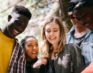 A group of diverse young adults enjoying a moment together outdoors, smiling and happy.