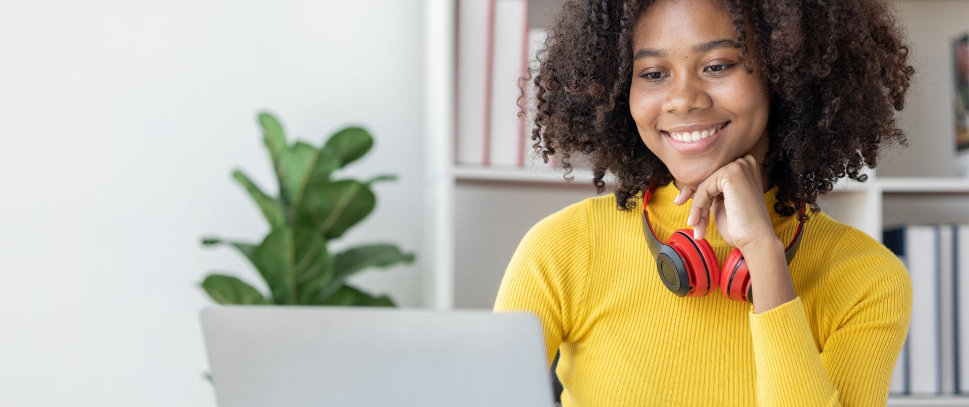 Teen girl in a green hoodie sitting at a desk, writing in a notebook, illuminated by sunlight.